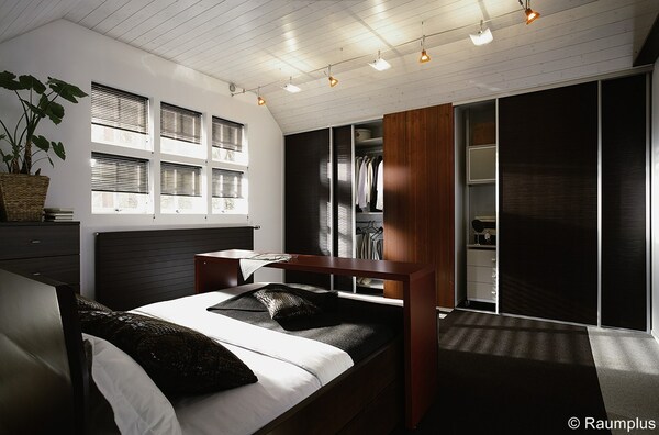 Modernes Schlafzimmer mit offenem Kleiderschrank, großen Fenstern und stilvollen Möbeln aus Holz.