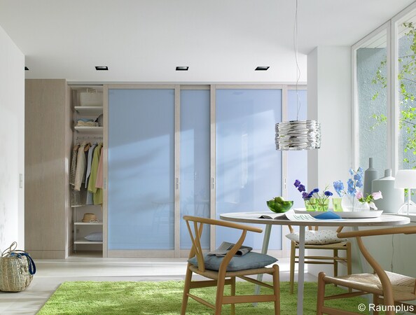 Helles Schlafzimmer mit modernem Kleiderschrank, Schiebetüren in Blau und gemütlicher Sitzecke.