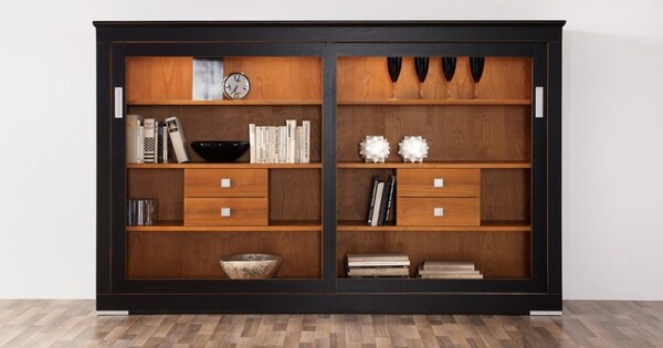 Modernes Regal aus Holz mit Schubladen, Büchern, Deko, Gläsern und Uhr auf Parkettboden.