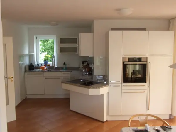 Moderne Einbauküche mit weißen Hochglanzfronten, Granit-Arbeitsplatte und Elektrogeräten.