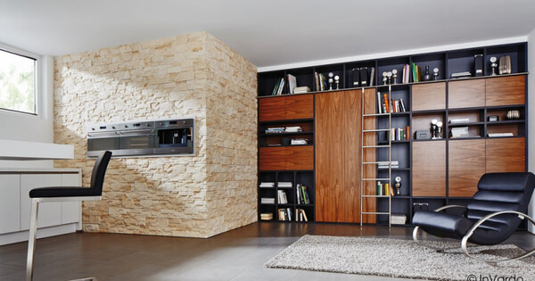 Modernes Wohnzimmer mit Bücherregal aus Holz, Ledersessel, Steinwand und gemütlichem Teppich.